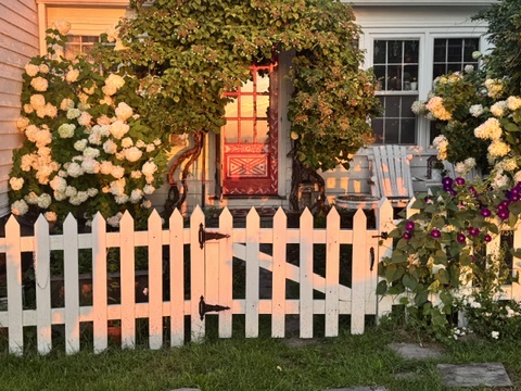 Flower-covered porch and white picket fence at sunset