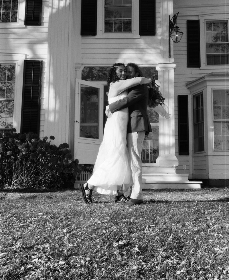 Black-and-white portrait of newlyweds embracing outside the house