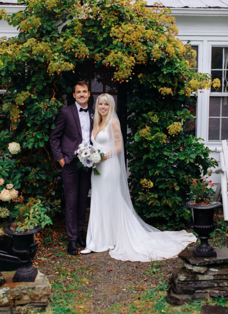 Newlyweds beneath flowering vines beside the house