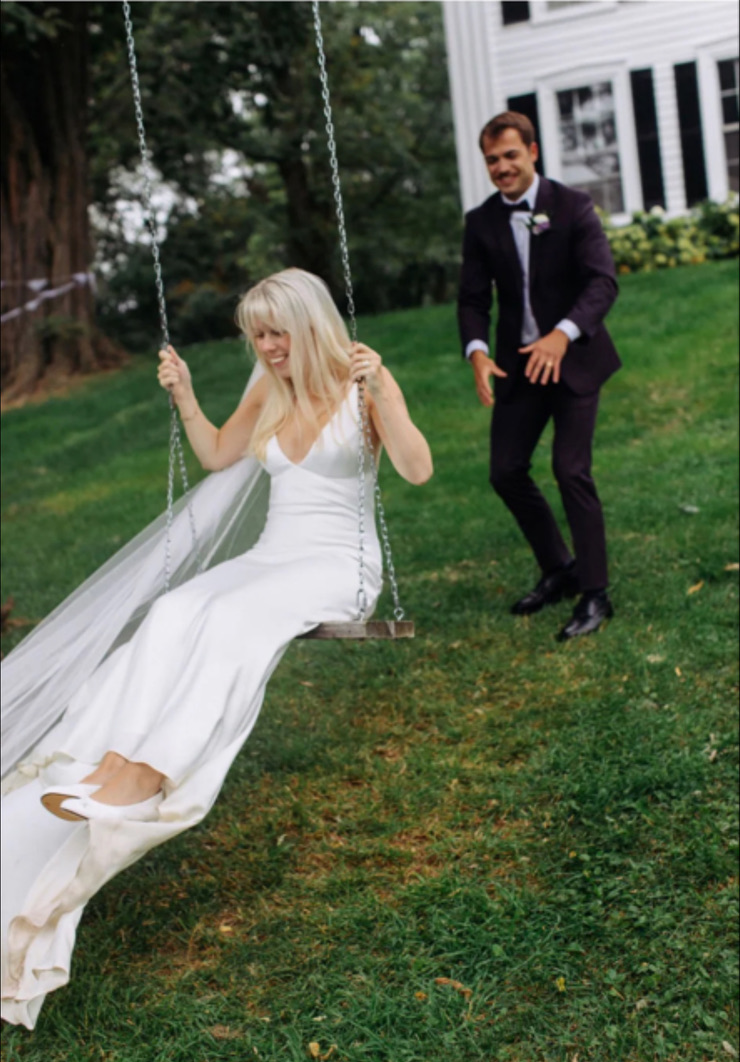 Bride on the tree swing with the groom behind her